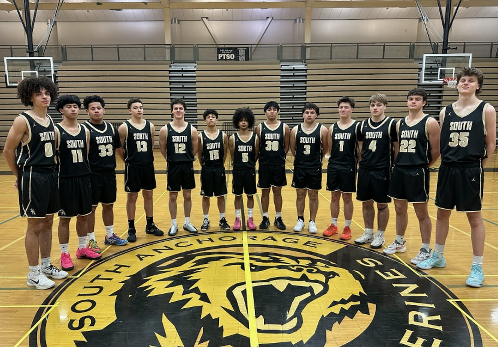 The 2025-26 South Anchorage varsity boys basketball team standing on the centre court crest
